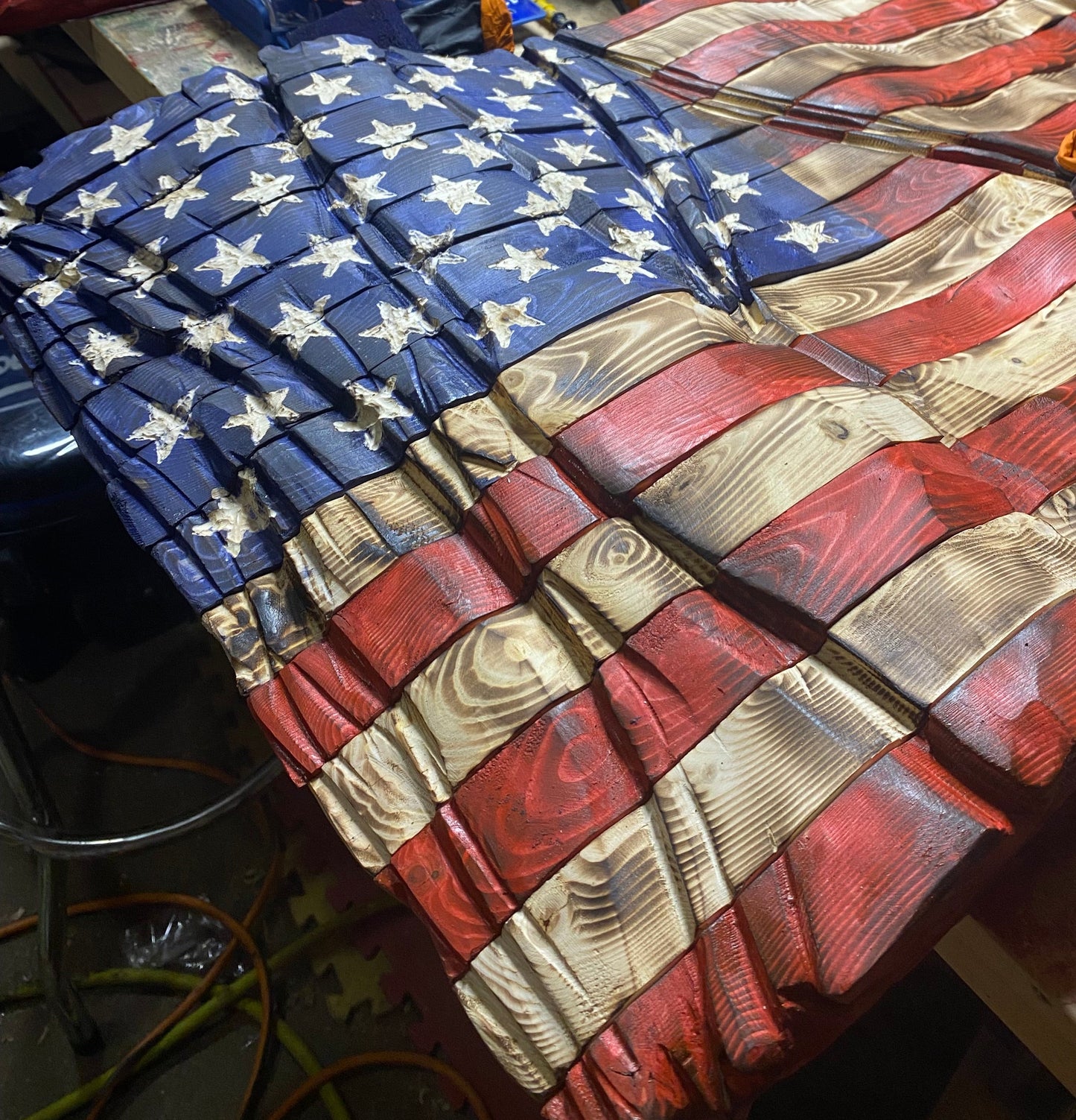 Wooden American flag sculpture with tools and materials in the background