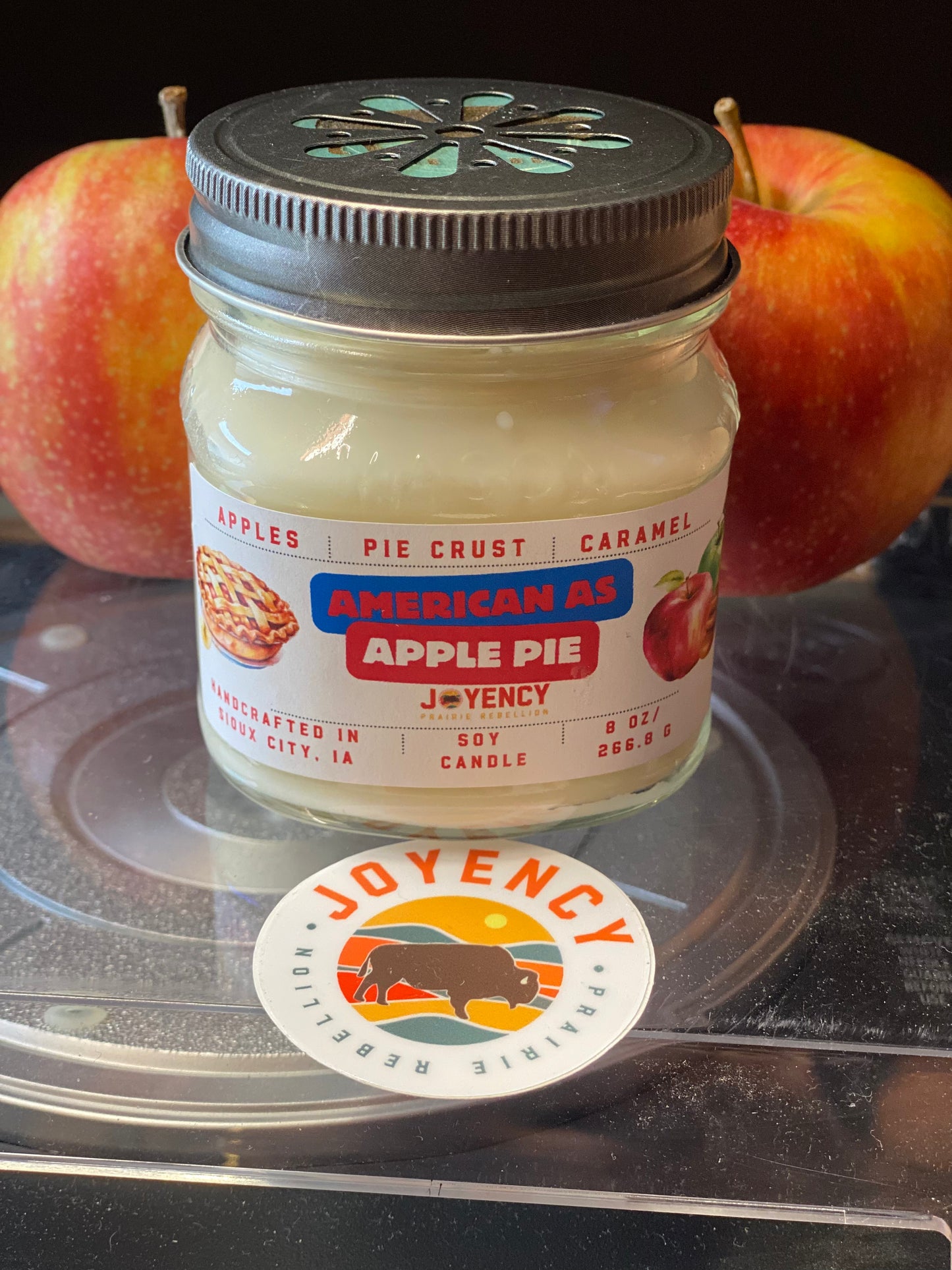 Jar of 'American as Apple Pie' candle by Joyency with apples in the background