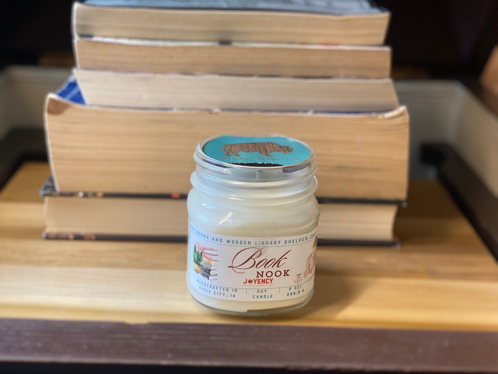 Jar of candle labeled 'Book Nook' with books stacked in the background