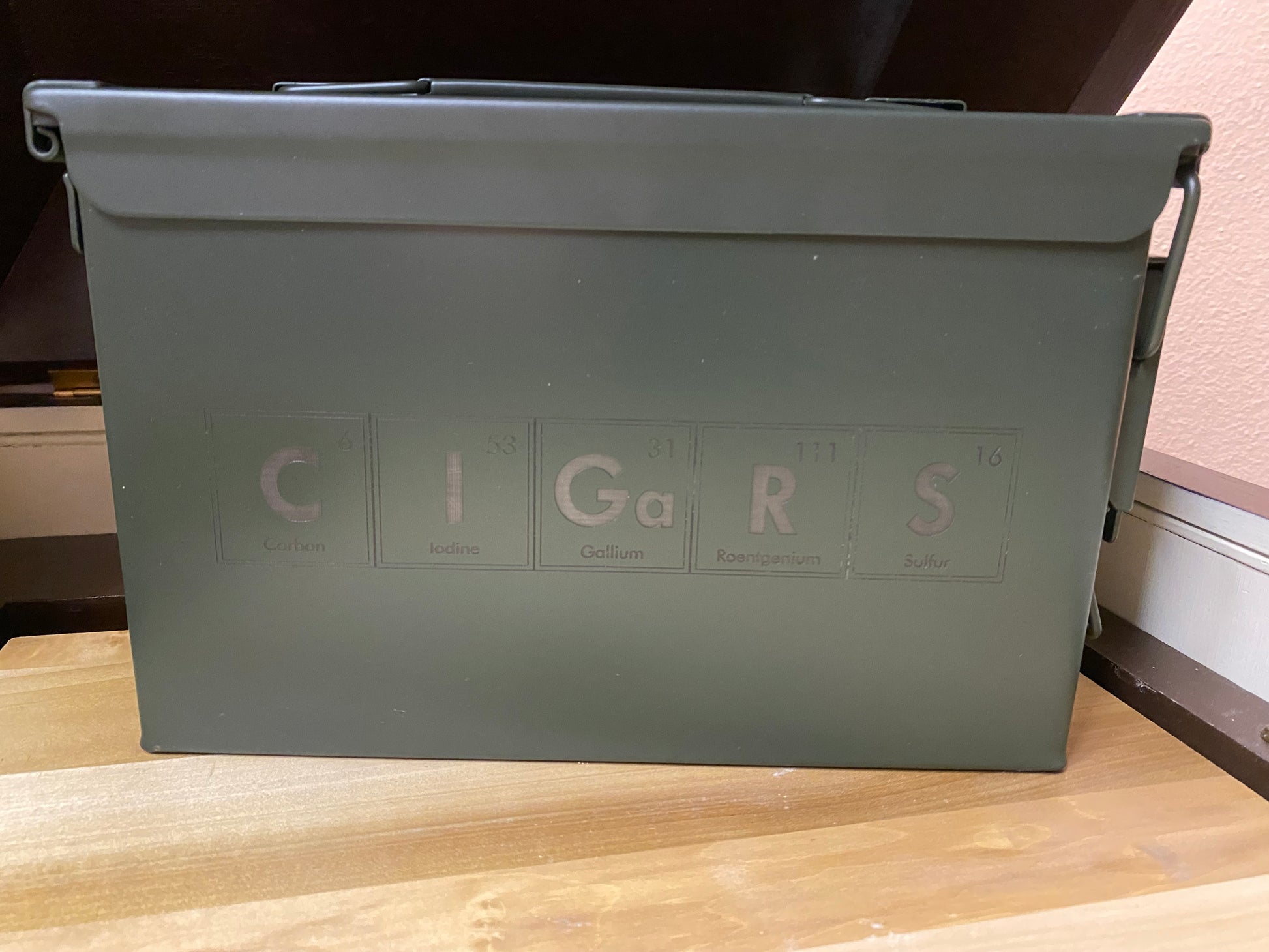Green metal box labeled 'CIGARS' on a wooden surface.