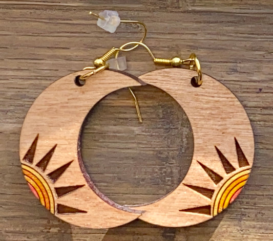 A wooden earring with a crescent shape featuring cut-out sunburst patterns in orange and yellow, attached to a gold-colored hoop and hook.