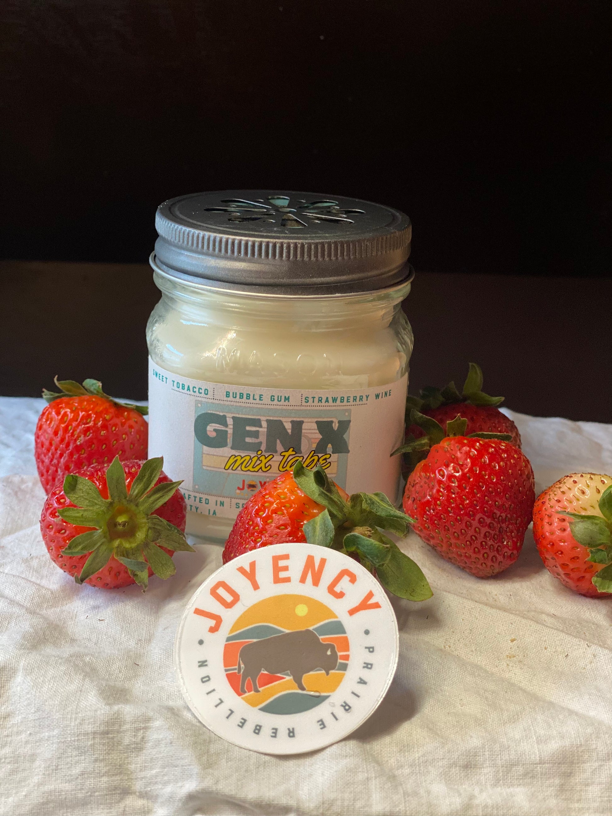 Jar of cream with a lid, surrounded by strawberries on a white cloth background