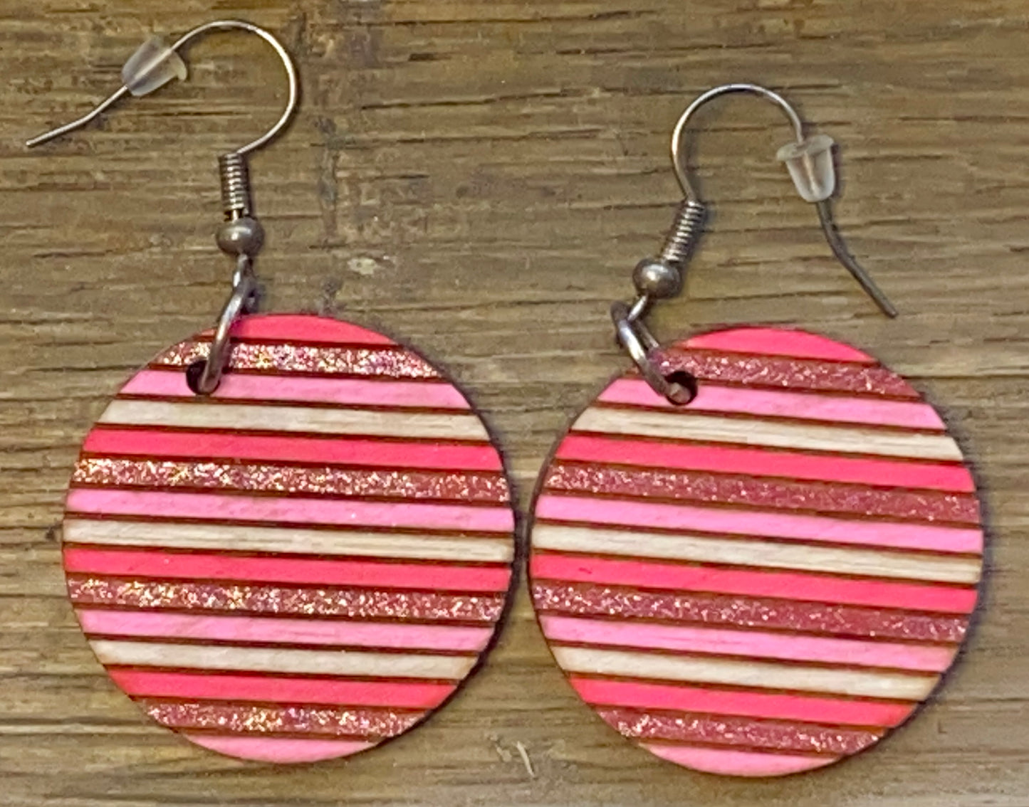 A pair of wooden circle earrings with red and gold stripes, attached to fishhook closures.