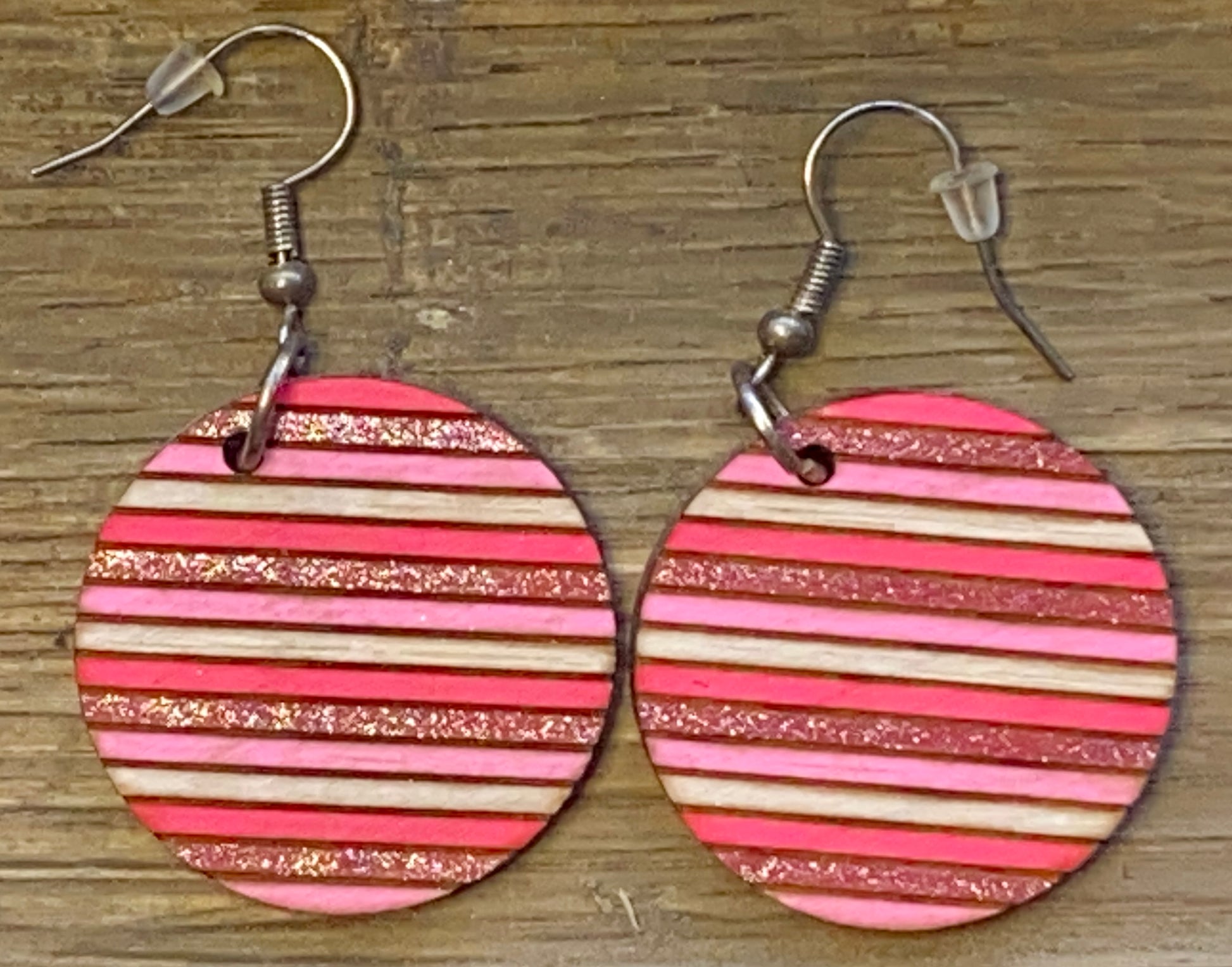 A pair of wooden circle earrings with red and gold stripes, attached to fishhook closures.