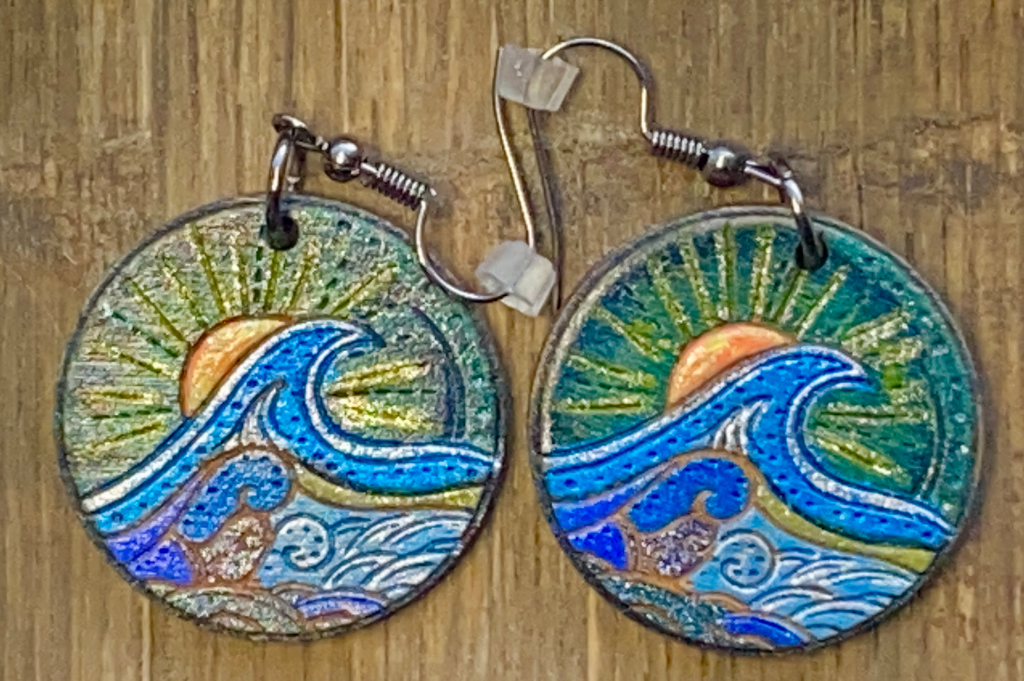 A pair of wooden earrings with a wave and sunset design in multiple colors.