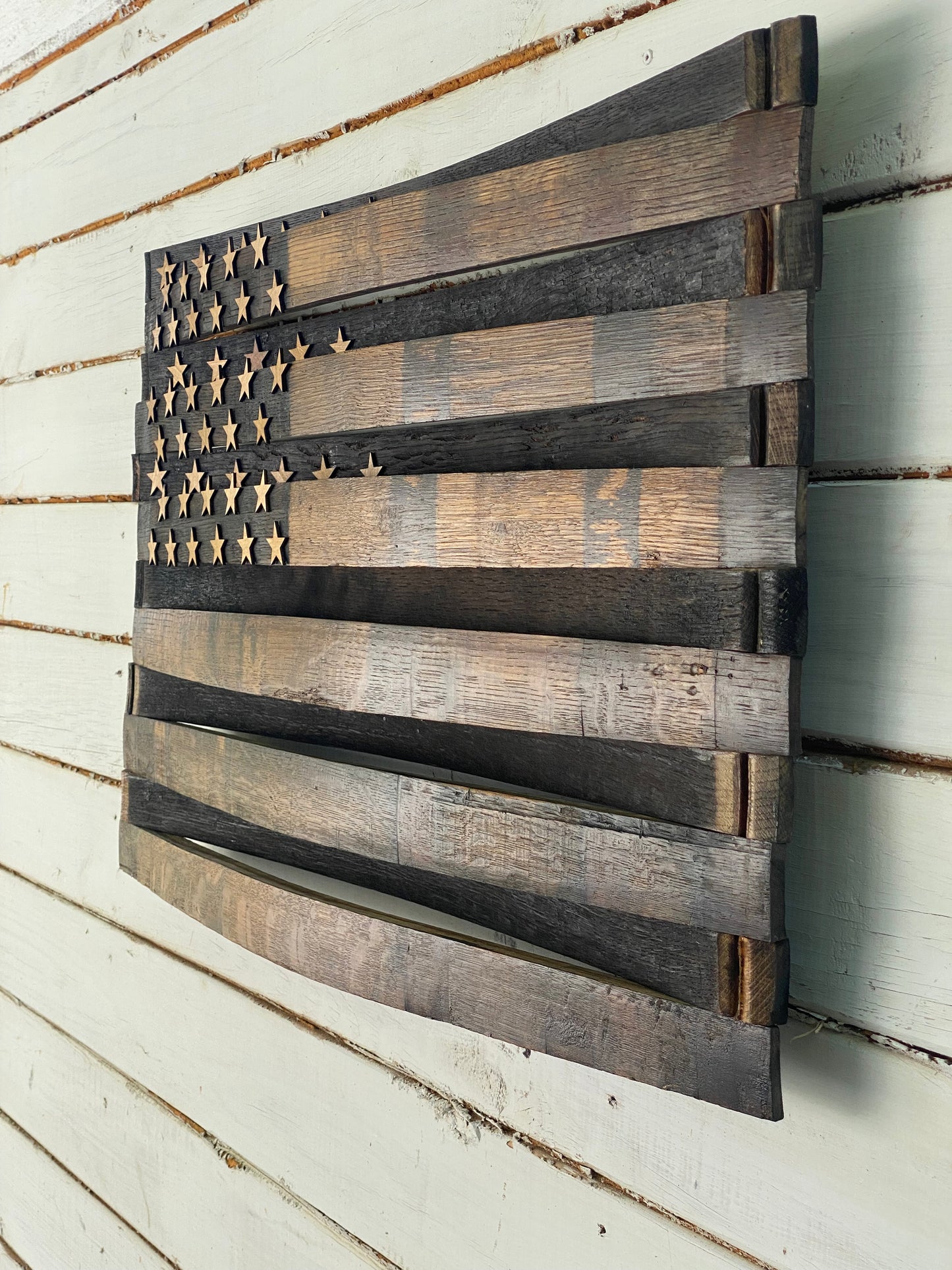 A rustic wooden American flag wall art piece made from reclaimed wood planks, mounted on a white painted wood plank wall.