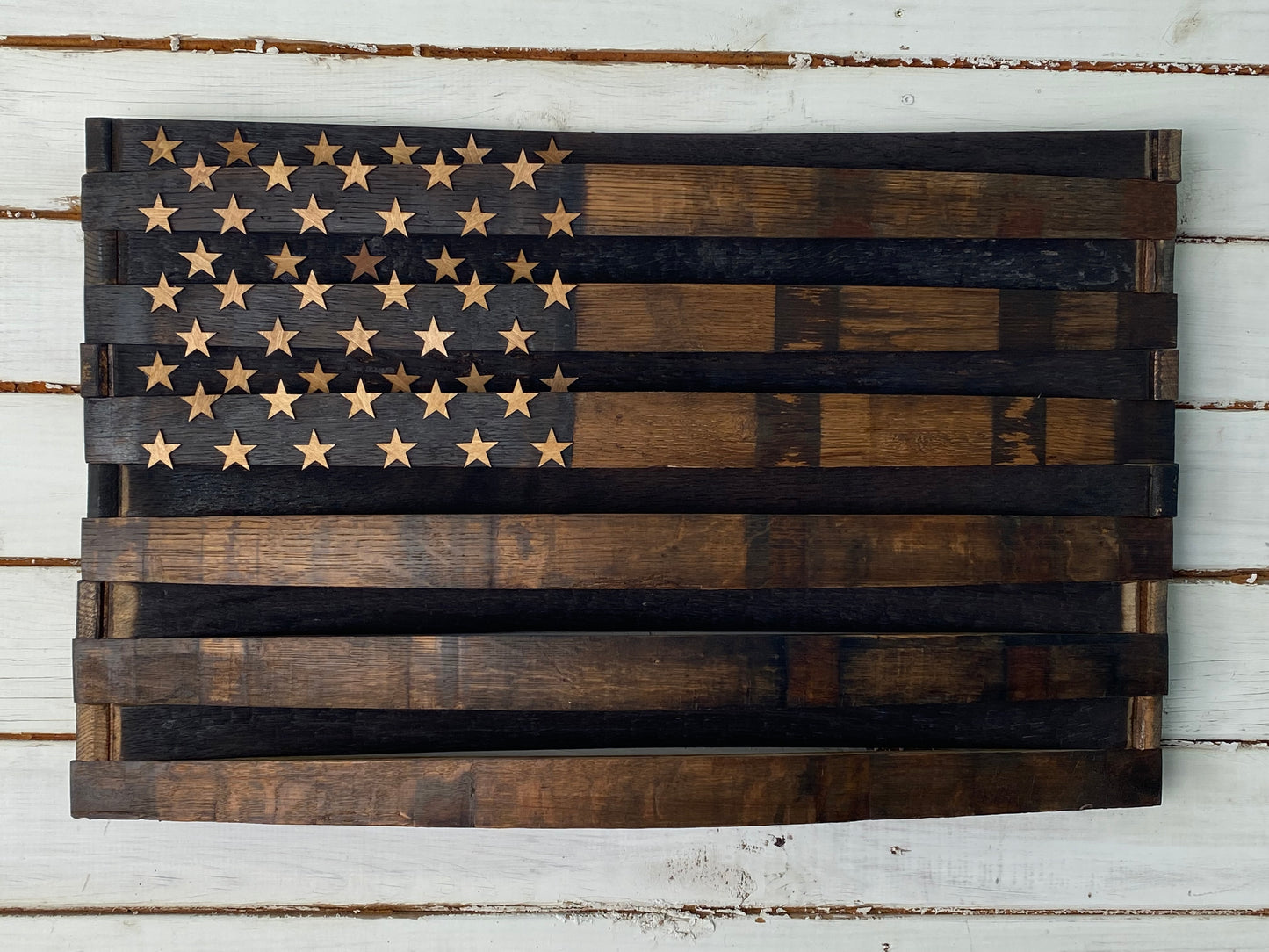 A rustic wooden American flag wall art piece made from dark stained wood planks, mounted on a white distressed wood plank background.