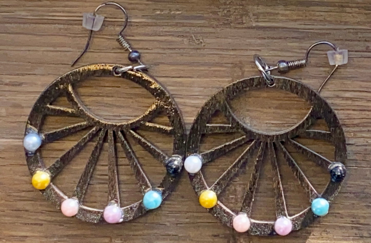 A pair of wagon wheel-inspired earrings with multicolored beads on a wooden surface.